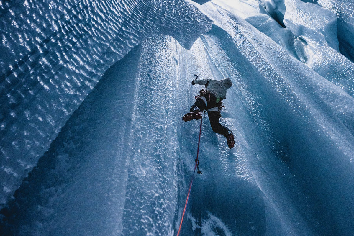 A climber geared up in Mammut equipment skillfully ascends a glistening ice wall using top-notch ice axes and ropes. The intricately textured ice sparkles under the light, showcasing the premium quality of Mammut's climbing gear.